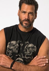 Schwarzes ärmelloses Shirt mit einem grauen Skull- und Schlangen-Graphic, begleitet von einem schwarzen geflochtenen Armband am Handgelenk. Nahaufnahme eines männlichen Modells.