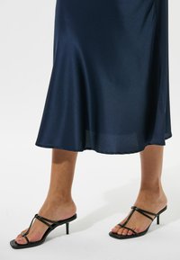 Navy Satin-Kleid mit einer glatten, glänzenden Textur, das knapp über dem Knie endet. Schwarze Absatzsandalen mit dünnen Riemchen und quadrater Zehenpartie.