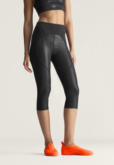 Kvinde iført sorte korte leggings og en matchende sports-bh, kombineret med lyse orange slip-on sportssko.