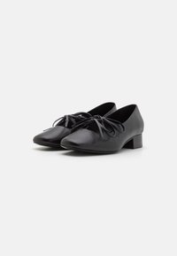 Zapatos de cuero negro con un tacón bajo en bloque, punta afilada y detalles de cordones en la parte delantera. Textura suave y diseño minimalista.