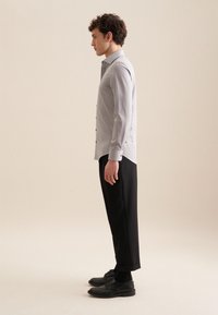 Lichtgrijze overhemden met lange mouwen, zwarte broek en zwarte schoenen. Het shirt heeft een slim fit en zwarte knopen, wat een strakke uitstraling creëert.