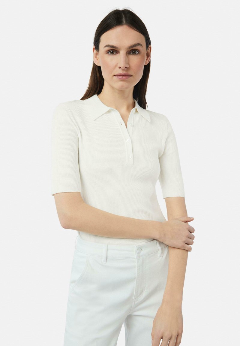 Weißes, geripptes Poloshirt mit kurzen Ärmeln und Knopfleiste, kombiniert mit hellen Hosen, die eine glatte, enganliegende Textur zeigen.