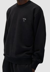 Felpa nera realizzata in tessuto morbido, con collo rotondo e polsini a costine. Logo bianco ricamato discreto sul petto, vestibilità comoda.