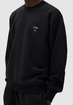 Felpa nera realizzata in tessuto morbido, con collo rotondo e polsini a costine. Logo bianco ricamato discreto sul petto, vestibilità comoda.