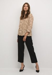 Beige Bluse mit Tierdruck und langen Ärmeln, kombiniert mit schwarzen, knöchellangen Hosen und schwarzen High Heels. Einfaches und lässiges Ensemble.