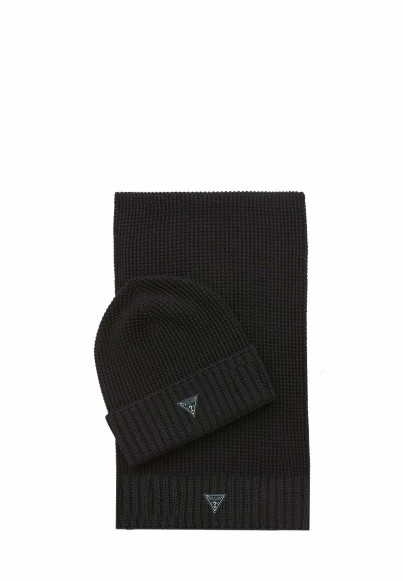Set composto da cuffia e sciarpa in maglia nera. La cuffia presenta una texture a coste con un risvolto piegato. Entrambi gli articoli sono decorati con una piccola toppa con logo.