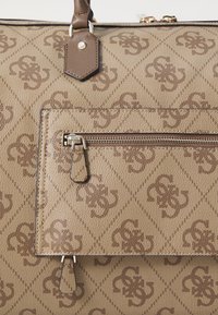 Brown canvas handbag with an abstract logo pattern, featuring a zippered pocket, leather accents, and sturdy top handles.