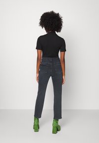 Jeans neri a vita alta con tasche posteriori, abbinati a una maglietta nera aderente e stivali in suede verde con tacco blocco, visti da dietro.