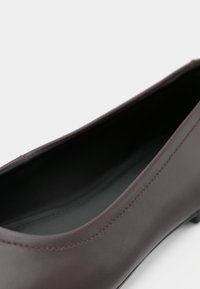 Primo piano di una scarpa piatta in pelle marrone scuro che mostra una texture liscia e una cucitura ben fatta lungo il bordo.