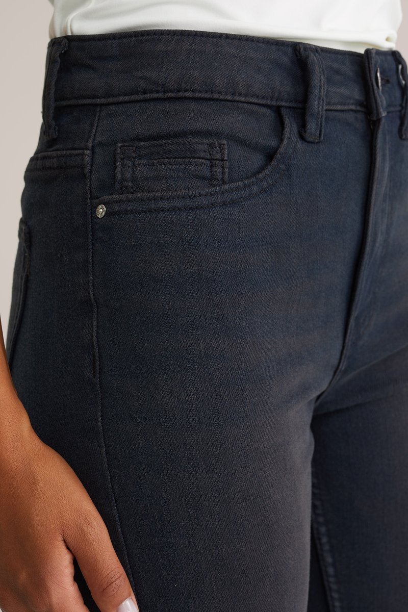 Temno modri kavbojki z tesnim fitom, ki imajo sprednji žep in podrobnost z kovinsko gumbom. Tkanina ima gladko teksturo.