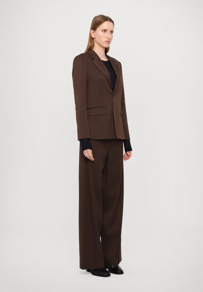 Brown tailored blazer with a single button, notched lapels, and two front pockets. Paired with wide-leg matching trousers and black shoes.