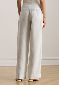 Fehér lenvászon bő szárú nadrág magas derékkal, két hátsó zsebbel és laza szabással, világos színű szandállal párosítva.