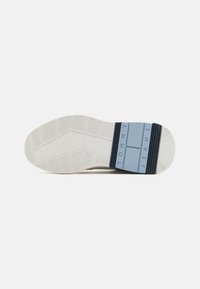 Suela blanca de goma con patrón texturizado, que presenta una banda azul clara etiquetada como "TOMMY JEANS" y un acento azul oscuro en el talón.