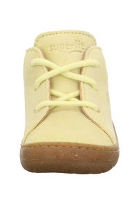 Geel suède schoen met rubberen zool, vetersluiting en subtiele roze accenten. "superfit" logo gedrukt op de tong.