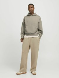 Felpa grigia con cappuccio e tasca frontale, abbinata a pantaloni beige a gamba larga e sneakers color miele con dettagli a motivo. Texture liscia e morbida.