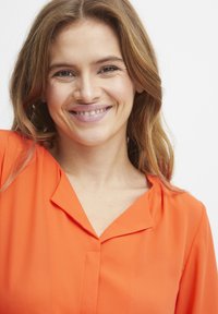 Orange blus med ett mjukt tyg, som har en sned krage och knapplist framtill. Designen har en avslappnad passform, lämplig för avslappnad klädsel.