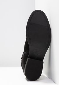 Semelle de chaussure habillée noire avec talon texturé et zone de l'avant-pied, couture visible et logo embossé "Vagabond" près de la voûte plantaire.