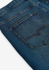 Jeans din denim de culoare albastru închis, cu o formă clasică; prezintă o buzunare pe spate cu un logo cusut și fire contrastante de culoare portocalie. Textură netedă.