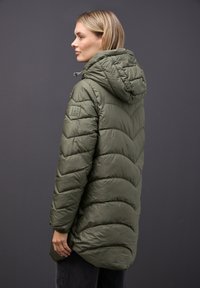 Chaqueta acolchada verde oliva con capucha, que presenta un diseño en forma de flecha y un parche texturizado en el hombro. Largo, con textura suave.