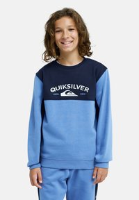 Sweat-shirt en polaire bleu et marine avec encolure ronde, manches longues et logo Quiksilver blanc. Texture douce, coupe décontractée, design casual.
