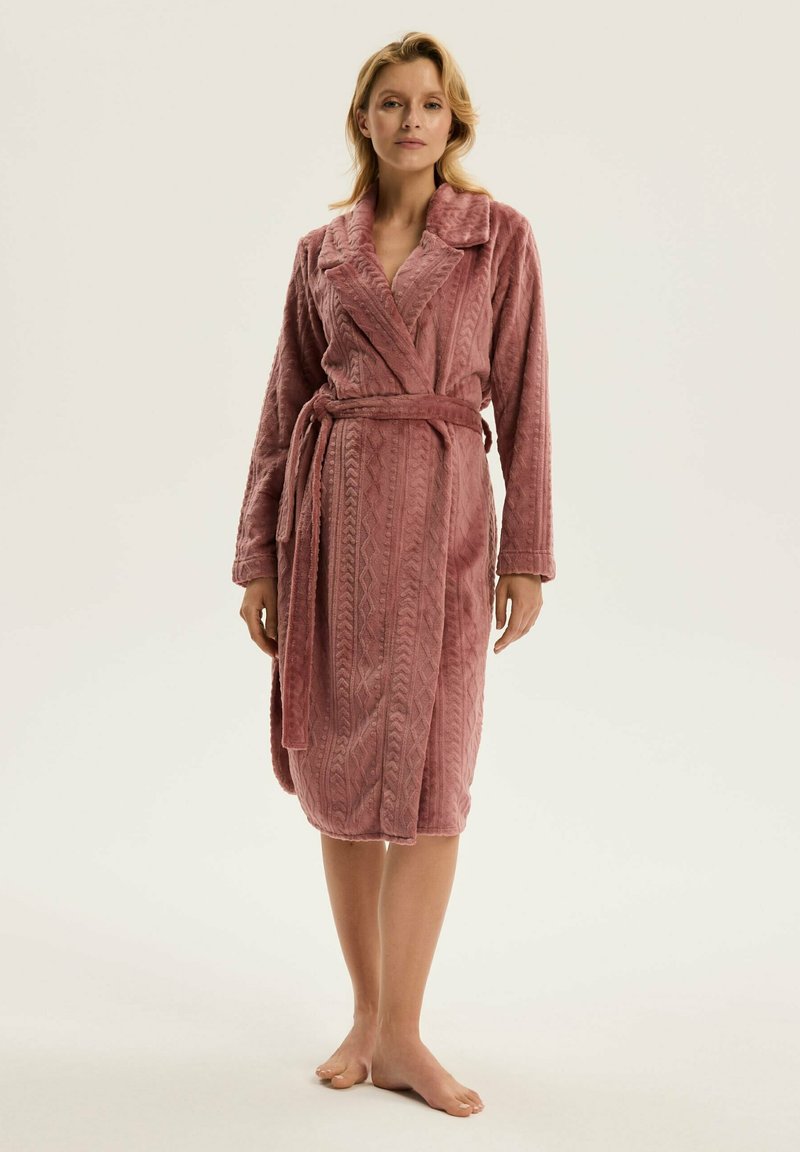 Różowy, strukturalny szlafrok z kołnierzem typu szal, wzorem tkanym, długimi rękawami i przewiązywanym paskiem, sięgający połowy łydki. Model bez obuwia.