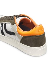 Grüner Wildleder-Sneaker mit weißen Lederakzenten, schwarzem Detail, orangefarbenem Fersenschild und strukturierter Gummisohle. Schnürsenkel und Innenmaterial in passendem Orange.