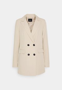 Beige dubbelknäppt kavaj med spetsiga slag, fyra svarta knappar, långa ärmar och två framfickor med klaff.