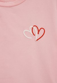 T-shirt rosa chiaro con due cuori sovrapposti, uno rosso e uno bianco, ricamati sul lato sinistro. Tessuto di cotone morbido, scollatura a girocollo.