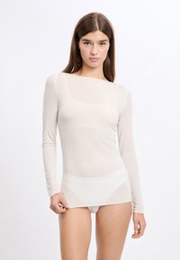 Top a maniche lunghe color beige chiaro in un tessuto morbido e trasparente, con scollo a barca e silhouette aderente, arricchito da sottili dettagli a coste.