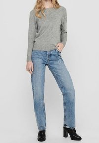 Maglione grigio a maniche lunghe, con scollatura rotonda e orlo a coste; abbinato a jeans dritti azzurri chiari e stivaletti neri con tacco a blocco.