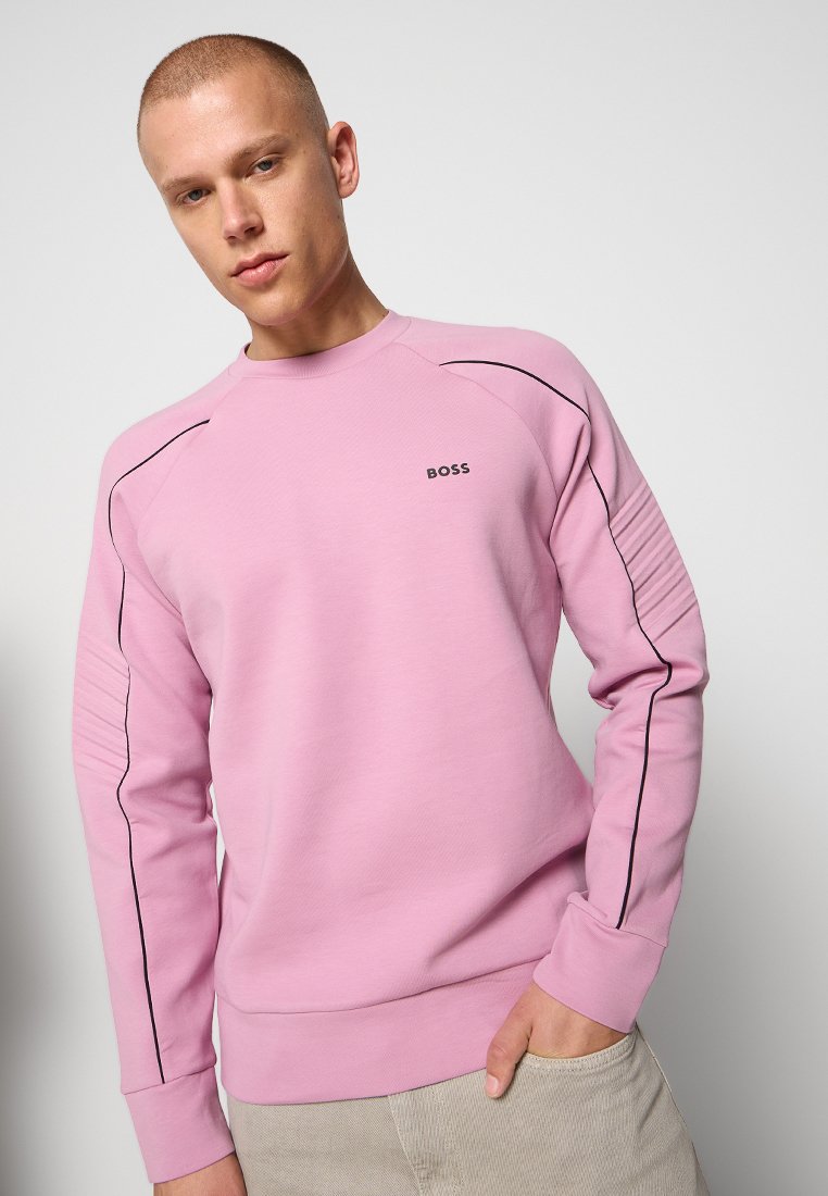 Sweatshirt rose clair en tissu texturé, avec des accents noirs le long des épaules et des manches, affichant un petit logo "BOSS" sur la poitrine.