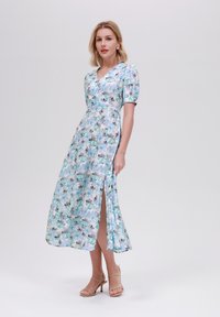 Maxiklänning med blommönster i nyanser av blått och grått, med V-ringning, puffärmar och en sidoklyvning för ökad rörelse.
