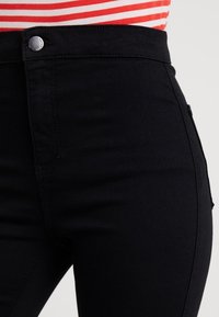 Černé džíny s vysokým pasem, vyrobené z elastického denimu, s přezkou na stříbrný knoflík a jemnými detaily v šití. Hladká textura a slim fit.