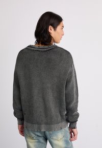 Oversized knit sweater in black and grey, featuring a ribbed texture, crew neck, and cuffed sleeves. The back is plain with a relaxed fit.