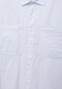 Jasnoniebieska koszula z guzikami, w kratkę, z dwiema przednimi kieszeniami i kołnierzykiem. Wykonana z teksturowanej tkaniny.