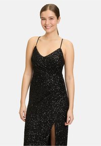 Schwarzes Paillettenkleid für den Abend mit V-Ausschnitt, dünnen Trägern und seitlichem Schlitz. Der Stoff hat eine strukturierte, glänzende Oberfläche mit gerafften Details im Oberteil.