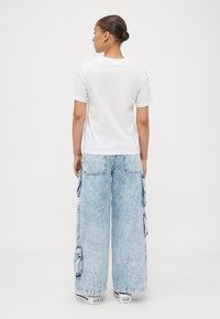 White cotton t-shirt with short sleeves paired with light blue wide-leg cargo jeans featuring side pockets and a loose fit.