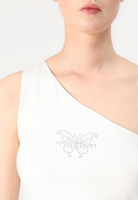 Hvit topp med én skulder og sommerfugldesign laget av rhinestener, med en jevn tekstur og en tettsittende silhuett.