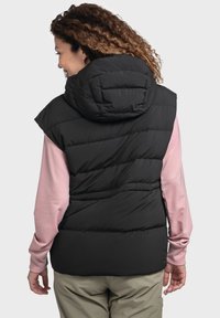 Schwarze Daunenweste mit Kapuze, mit einem gesteppten Muster und ärmellosem Design, getragen über einem hellrosa Langarmshirt.