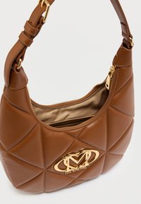 Καφέ τσάντα ώμου από συνθετικό δέρμα με υφή διαμαντένιας ραφής, χρυσά μεταλλικά στοιχεία και εμφανές λογότυπο στο μπροστινό μέρος. Κλείσιμο με φερμουάρ στην κορυφή.