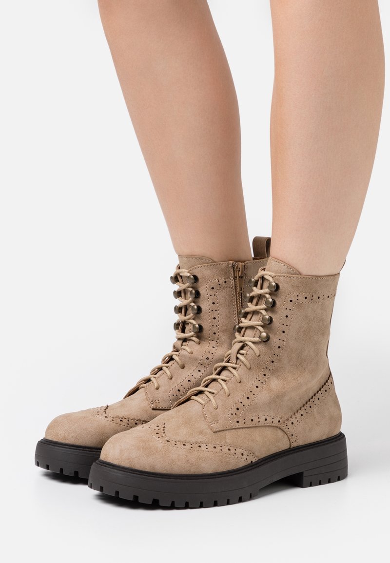 Beige mocka snörstövlar med brogue-detaljer, sidodragkedja och en tjock svart gummisula för förbättrat grepp.