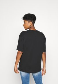 T-shirt nera oversize con maniche corte, collo rotondo e texture morbida in cotone, indossata con jeans blu, vista da dietro.