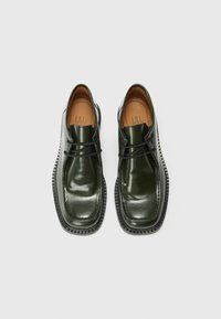 Green patent leather shoes with a smooth finish, featuring black laces, a rounded toe, and a textured sole. Brown insole visible inside.
