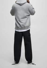 Szara bluza z kapturem o miękkiej fakturze, z kapturem i prążkowanym wykończeniem. Połączona z czarnymi spodniami cargo, również w luźnym kroju i z elastycznymi mankietami.