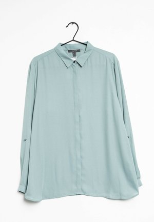 Hellblaues, langärmeliges Hemd mit Knöpfen und spitzem Kragen, das an einem schwarzen Kleiderbügel vor weißem Hintergrund hängt.