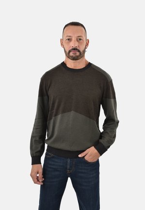 Dunkelgrüner und grauer Pullover mit geometrischem Muster, Rundhals-Ausschnitt und gerippten Bündchen und Saum, getragen über dunklen Jeans.
