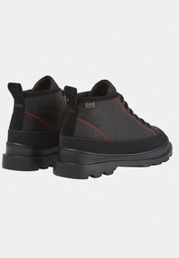 Scarpe nere con tessuto testurizzato, cuciture rosse a contrasto e suole in gomma spesse. Include linguette per la presa e design con lacci.