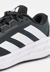 Melnas sporta kurpes ar elpojošu acs augšdaļu, trim baltām svītrām un mīkstu balto zoli ar teksturētām akcentiem.
