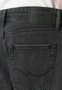 Svarte denim jeans med baklomme og midjebånd med svart lærmerkelapp merket "JACK & JONES" og sømdetaljer.