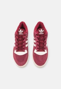 Burgundski suede tenisice s bijelim kožnim naglascima i tri pruge. Imaju zaobljen vrh, vezivanje i potpisani logo na jeziku.